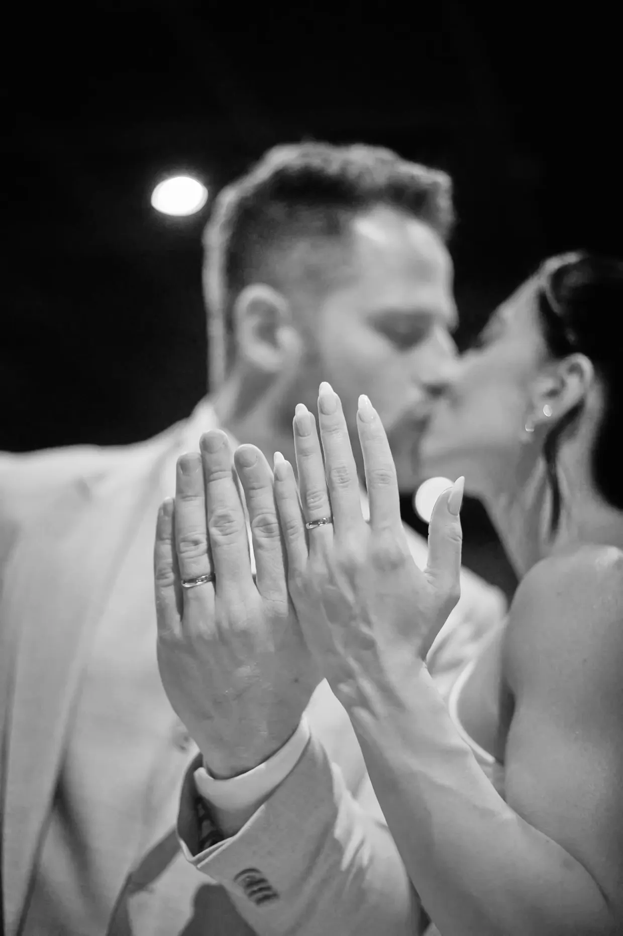 Fotografia em preto e branco de um casal se beijando, com as alianças em primeiro plano.