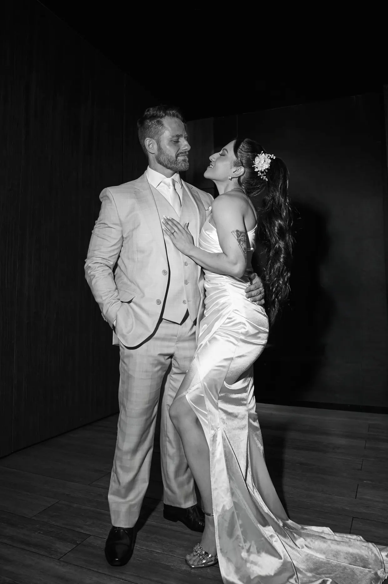 Casal em traje de festa posa junto em um ambiente escuro, em preto e branco.