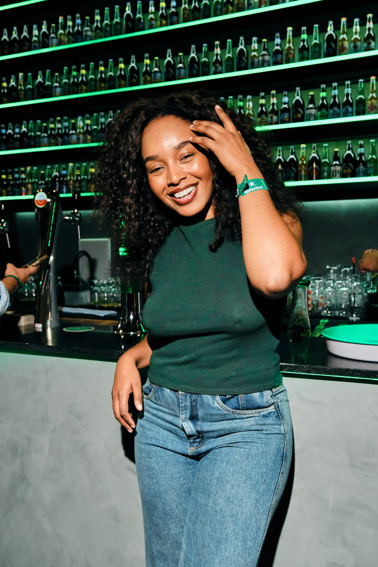 Mulher de blusa verde sorri diante de um balcão iluminado em verde.