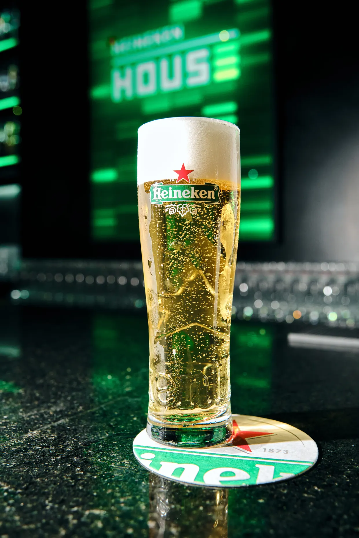 Copo alto de cerveja sobre um balcão, com iluminação verde ao fundo.