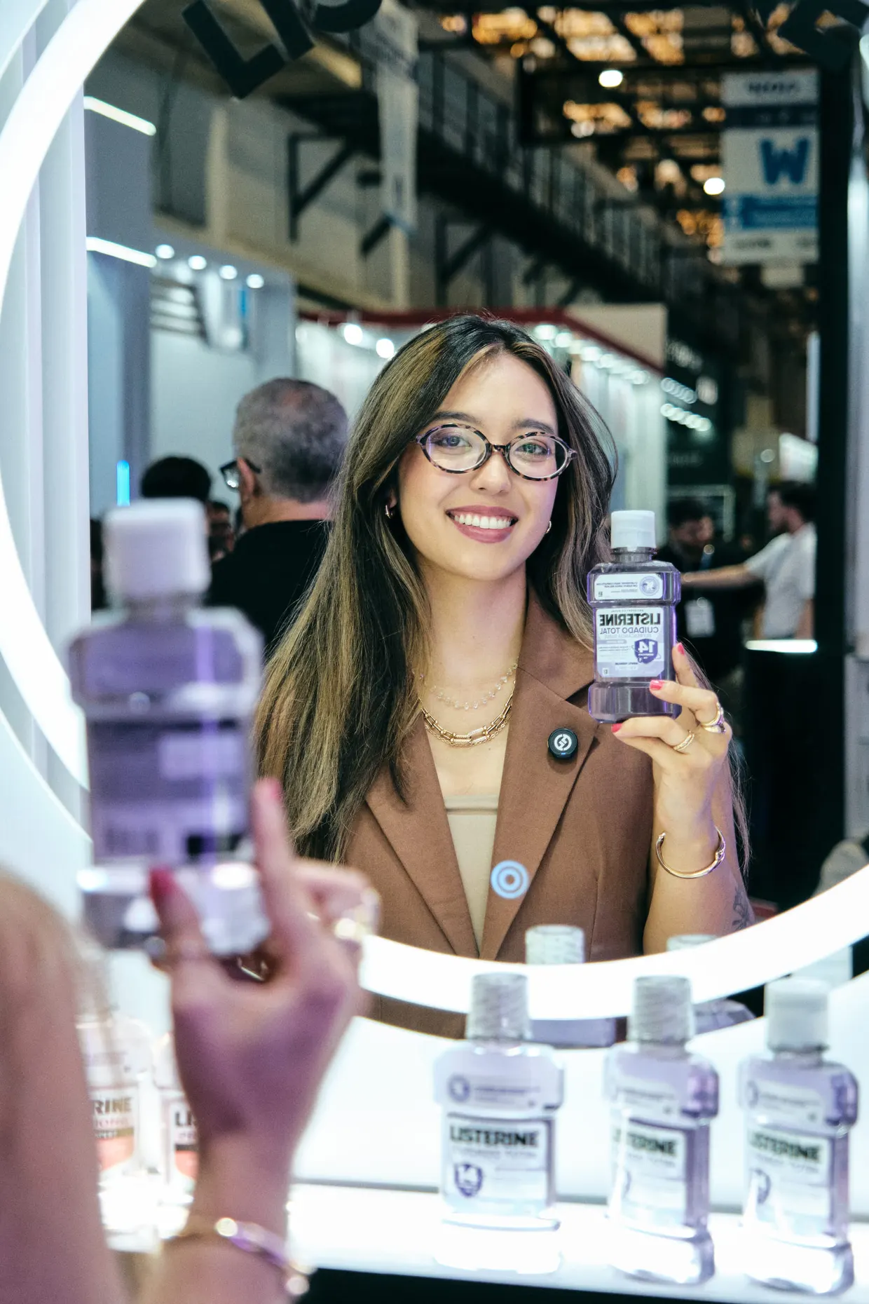 Mulher de óculos sorri diante de um espelho em um estande de produtos.