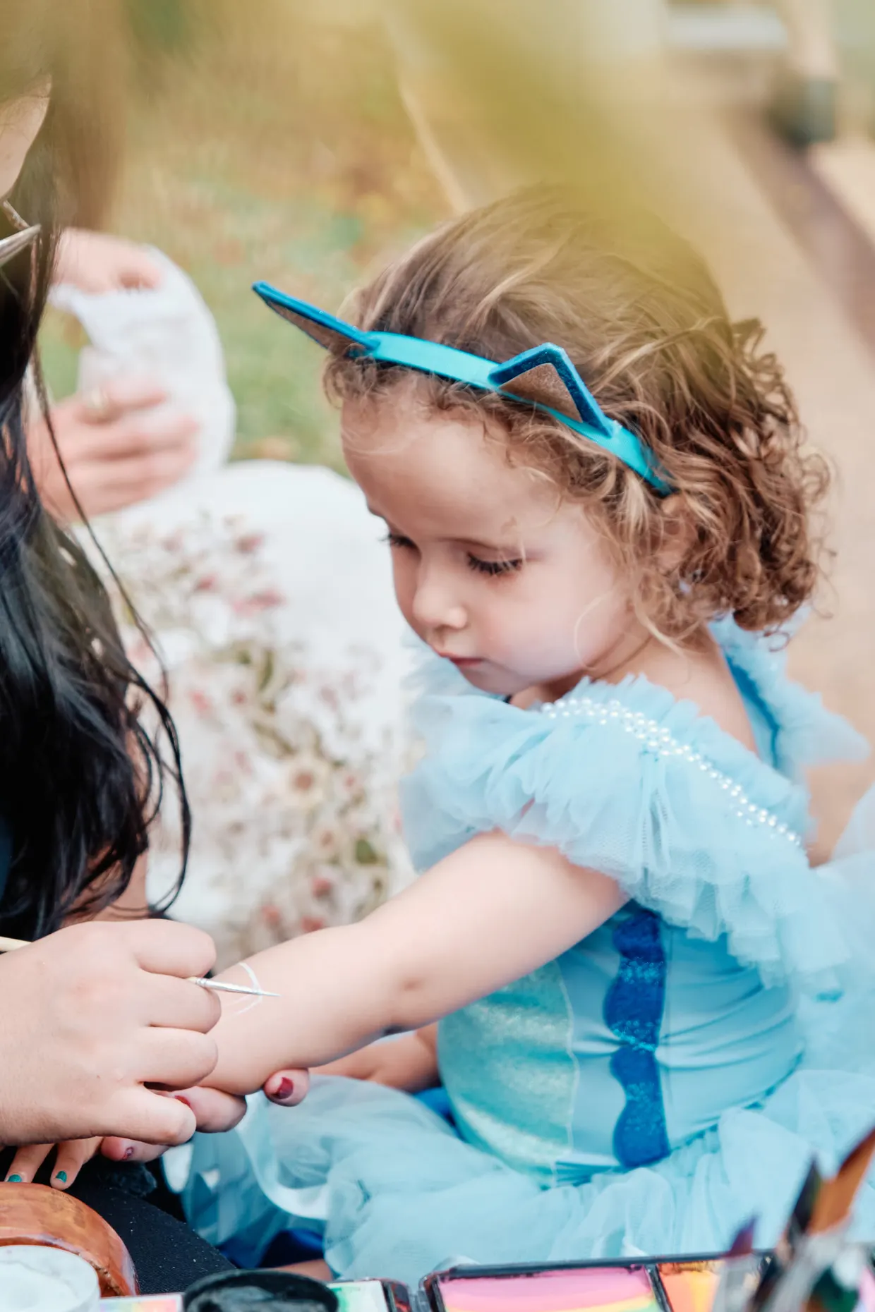 Criança de vestido azul e tiara brinca durante uma festa de aniversário.