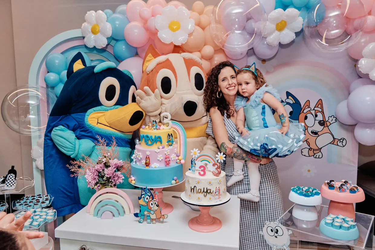 Mulher e criança posam atrás da mesa de aniversário, cercadas por doces e personagens.