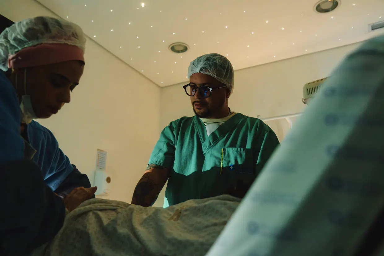 Pessoas de roupa hospitalar acompanham o parto ao lado da cama.