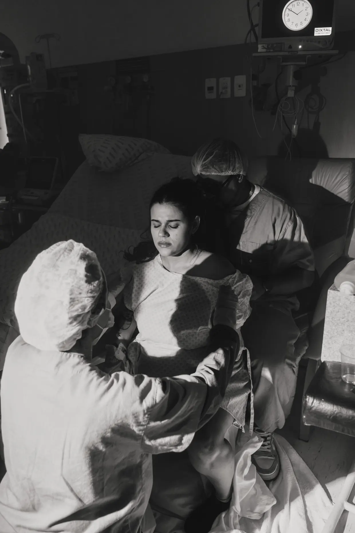 Mulher recebe apoio de uma pessoa de roupa hospitalar ao lado da cama.