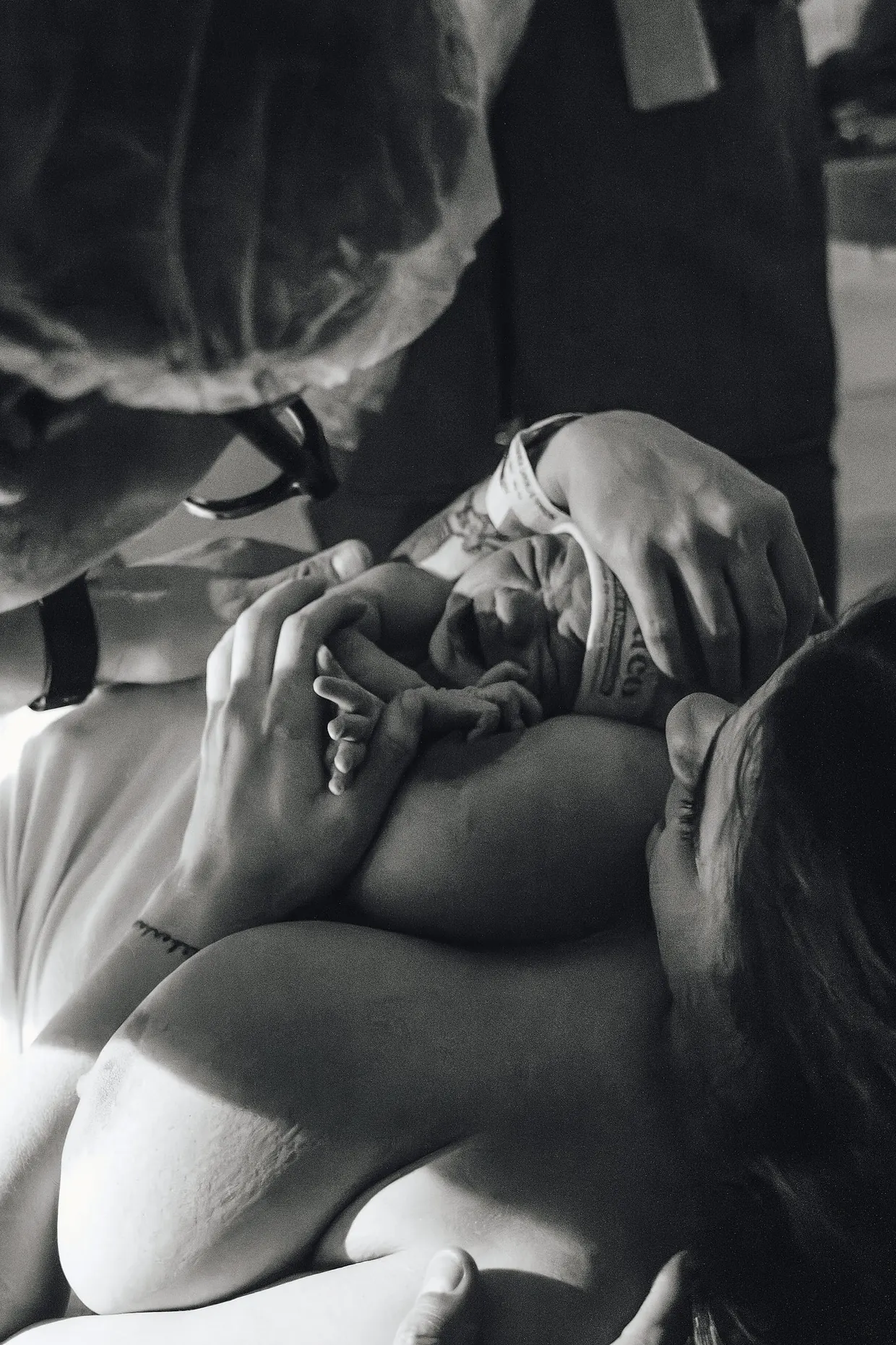 Fotografia em preto e branco de recém-nascido acolhido junto ao peito da mãe.