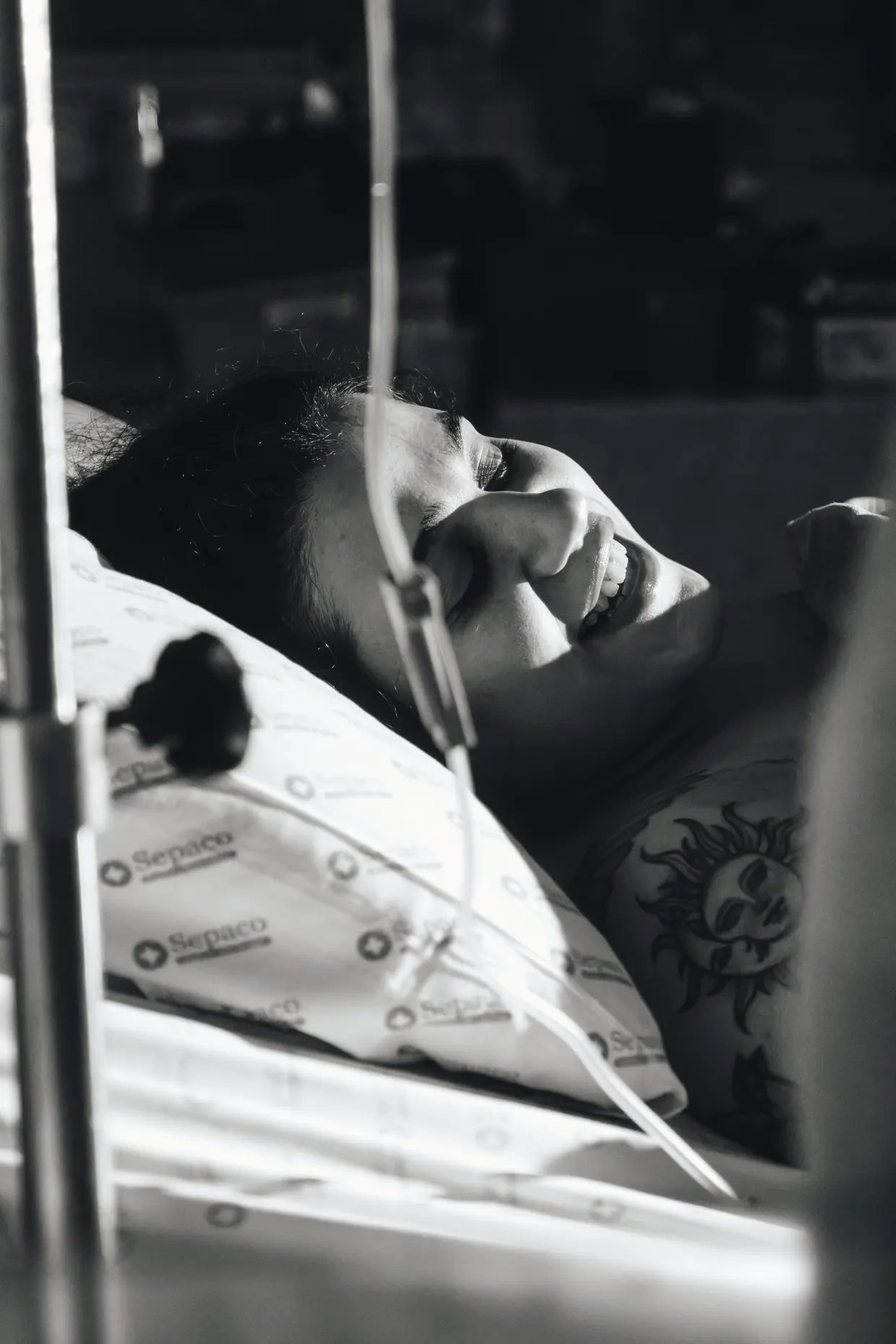 Fotografia em preto e branco de mulher reclinada na cama do hospital.