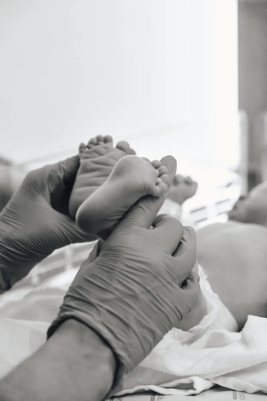 Close em preto e branco dos pés de um recém-nascido amparados por mãos com luvas.