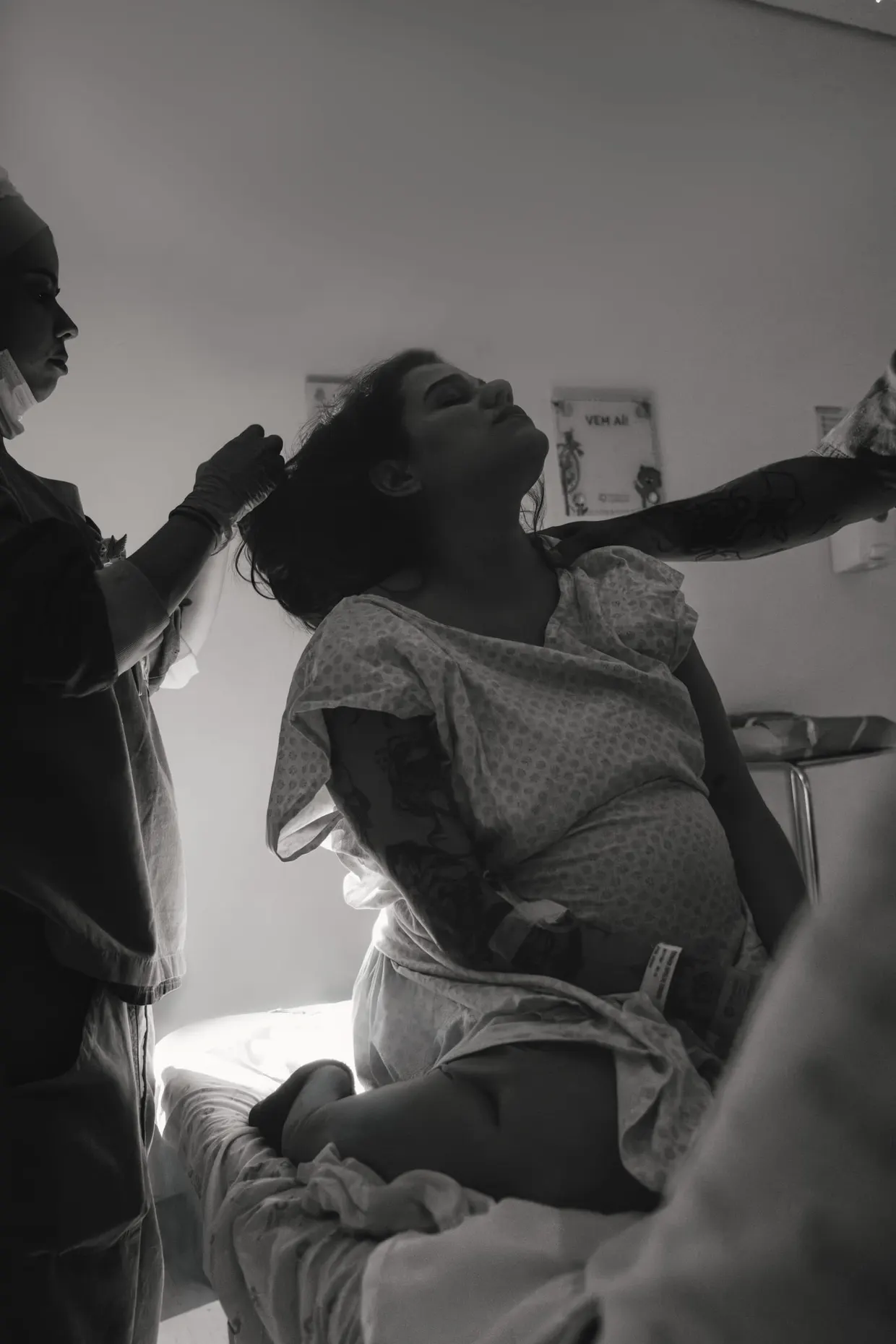 Mulher recebe apoio ao lado da cama hospitalar, em fotografia em preto e branco.