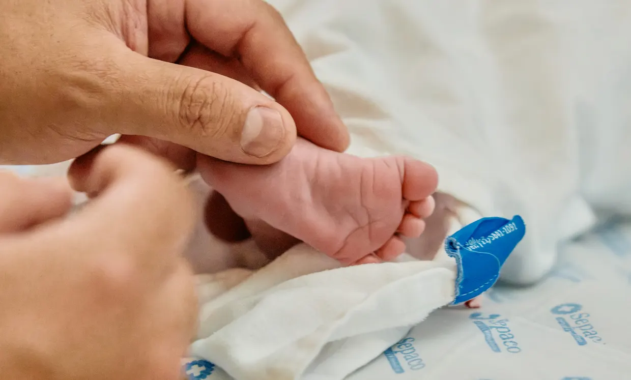 Close dos pés de um recém-nascido tocados delicadamente por mãos adultas.
