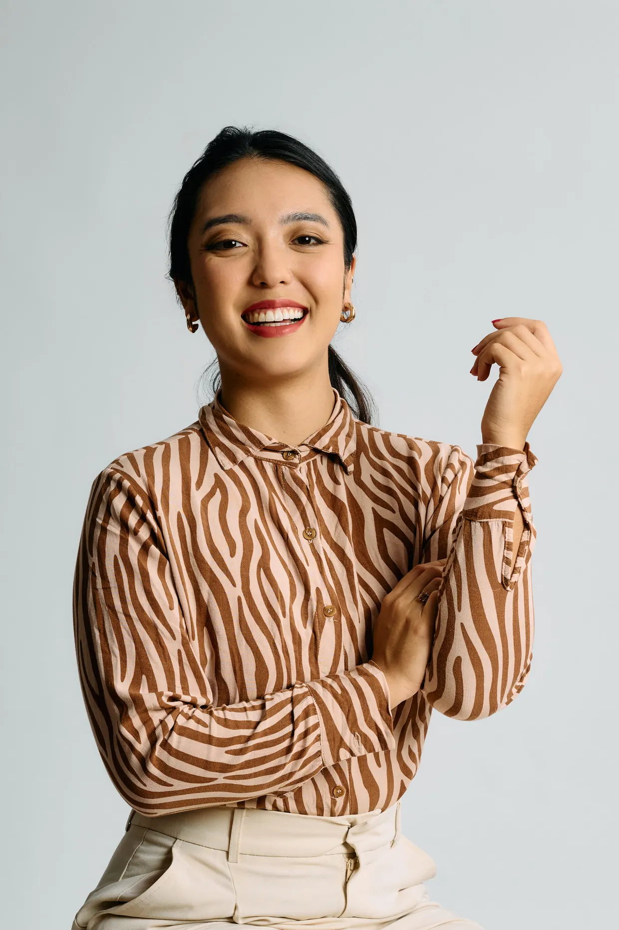 Retrato de mulher sorrindo, com blusa estampada e uma das mãos levantada.