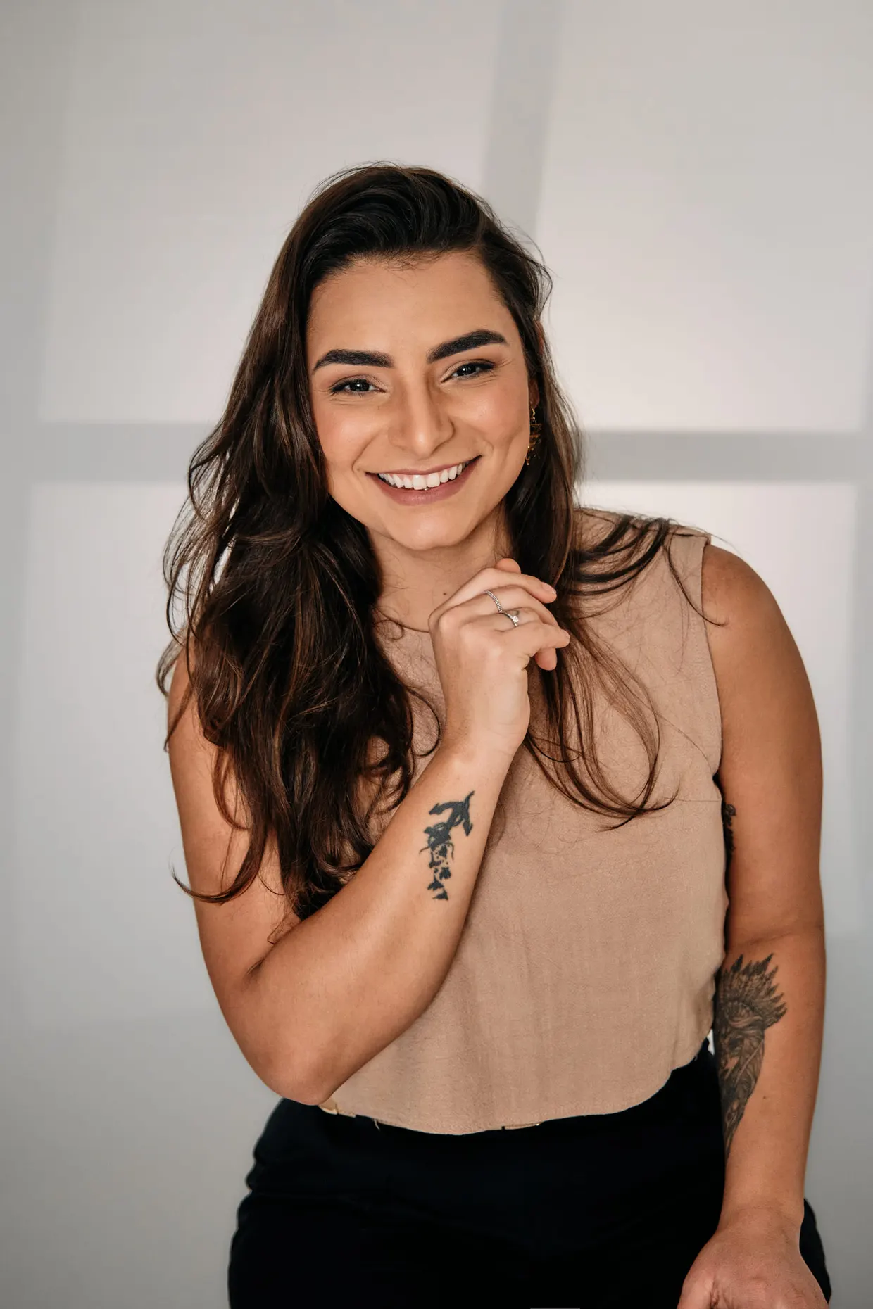 Mulher de blusa bege posa sorrindo, com uma das mãos junto ao rosto.