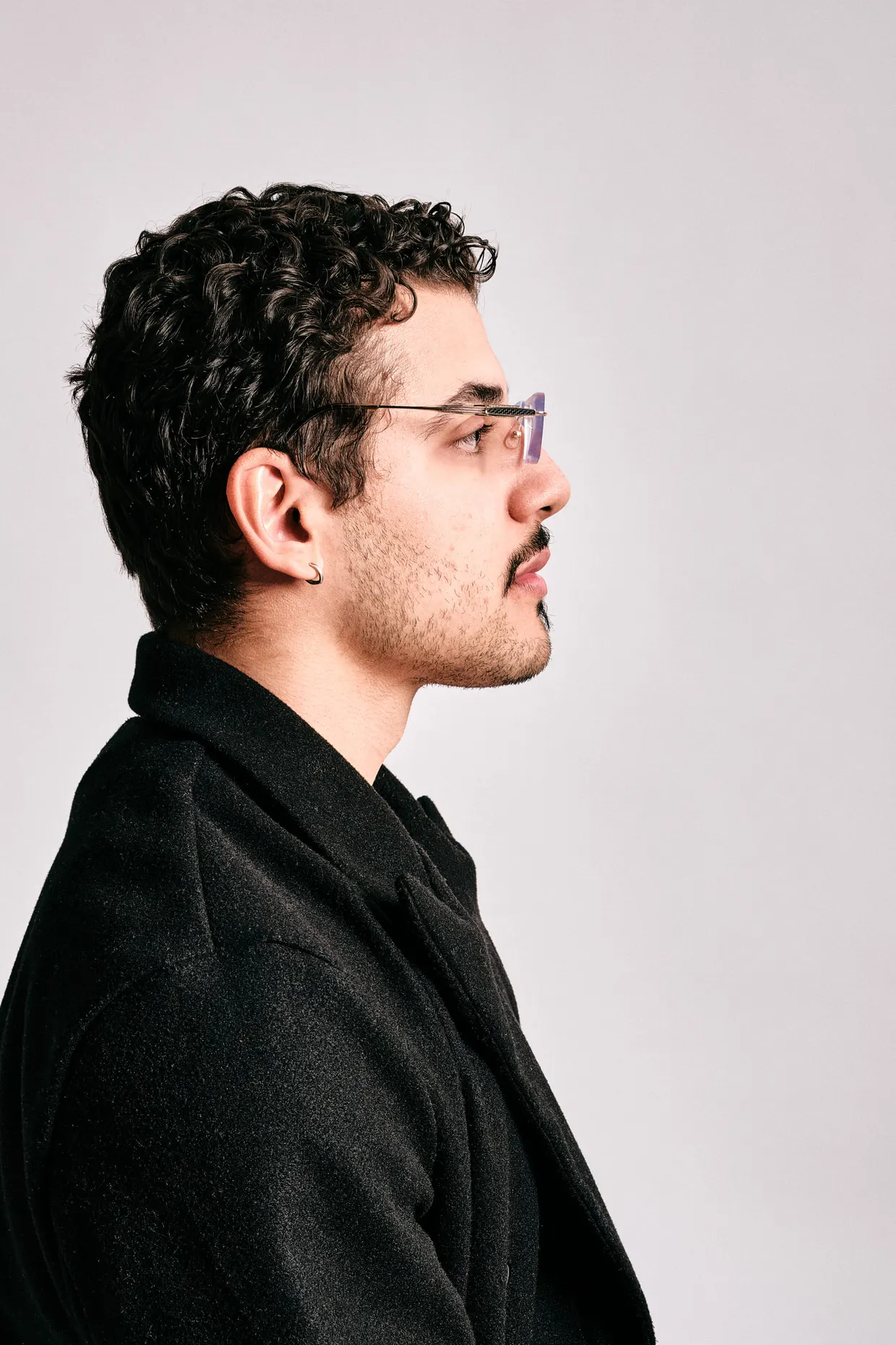 Retrato de perfil de homem com óculos e camisa preta, diante de fundo claro.