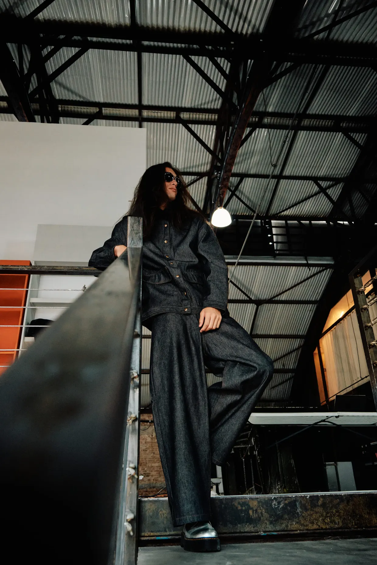 Modelo com roupa escura e botas prateadas posa em uma escada metálica.