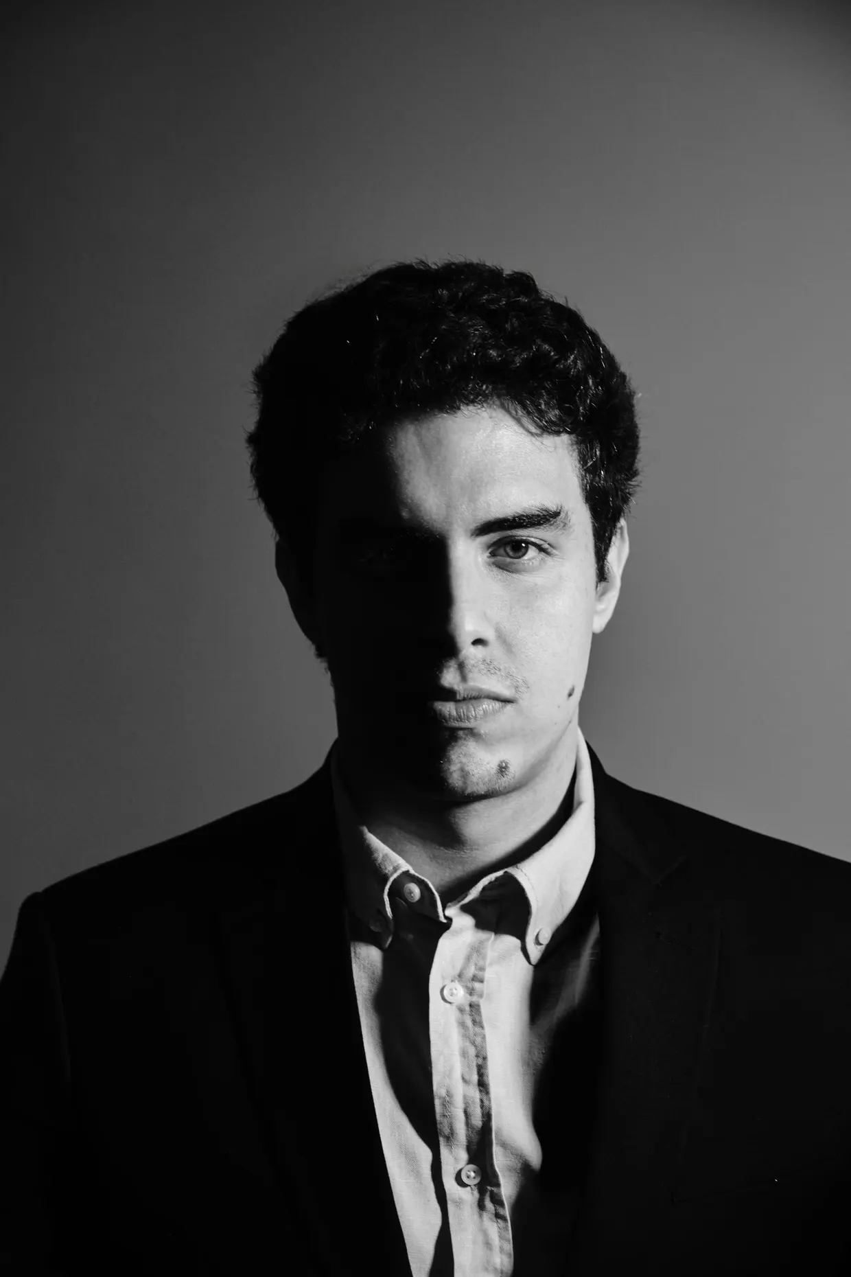Retrato em preto e branco de homem de terno, com iluminação lateral e fundo cinza.